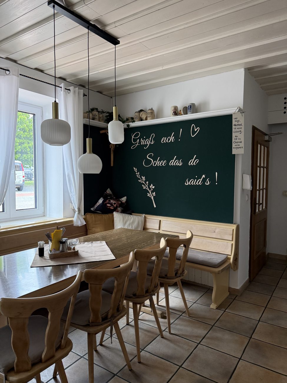 Gemütlicher Gastraum mit grüner Wand und dem Schriftzug „Griaß eich! Schee das do said's!“